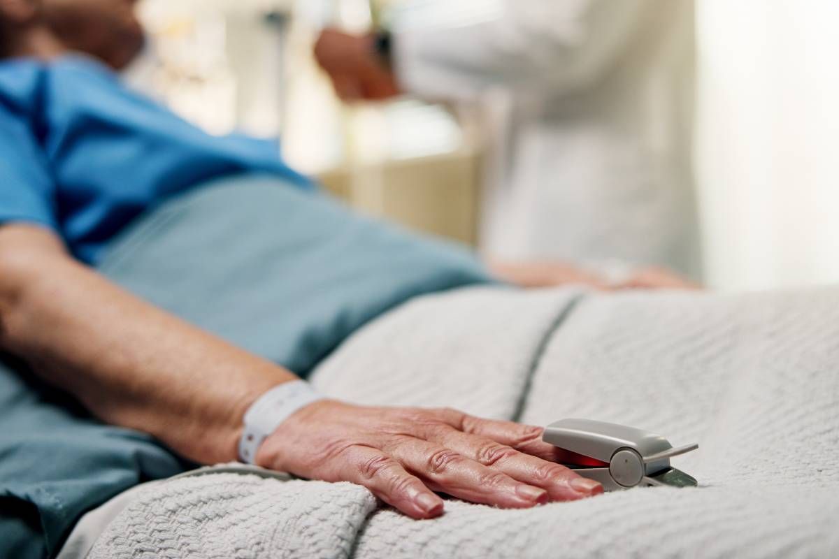 A chronically ill patient resting in bed with a doctor in the background