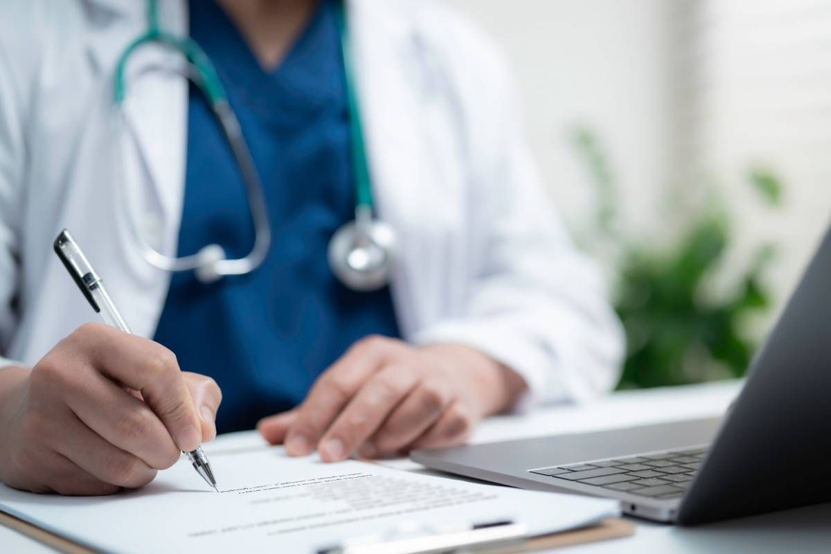 A doctor writing notes on medical paperwork at a desk.