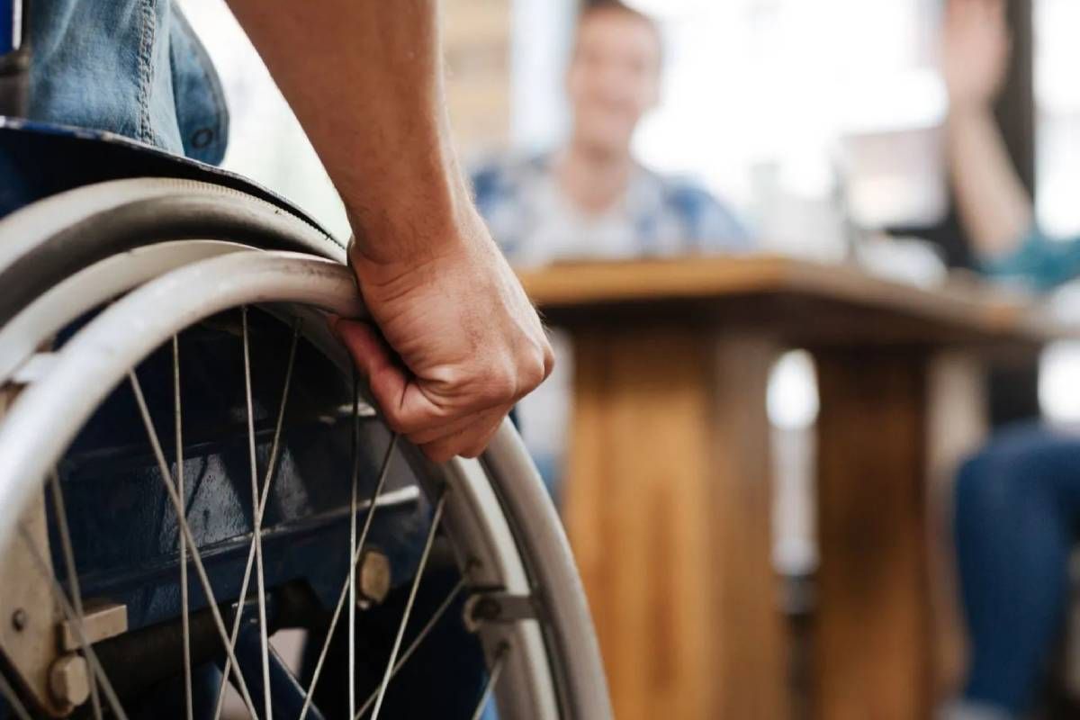 A person in a wheelchair approaching others seated at a desk.