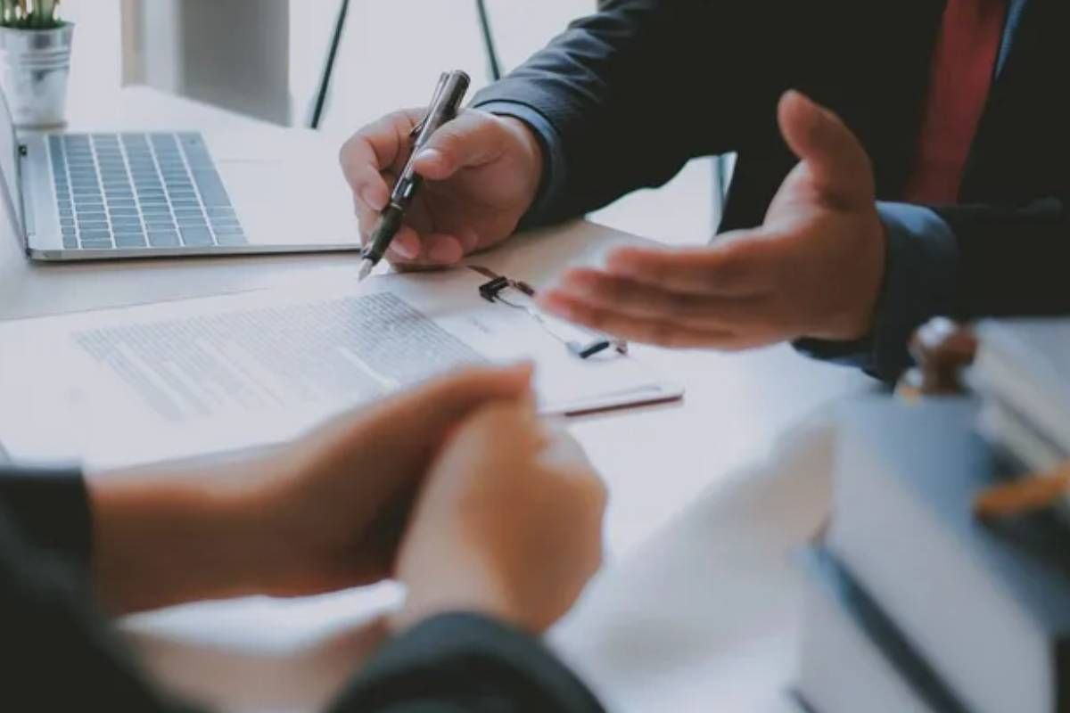 Someone writing on a document with a pen in front of another person