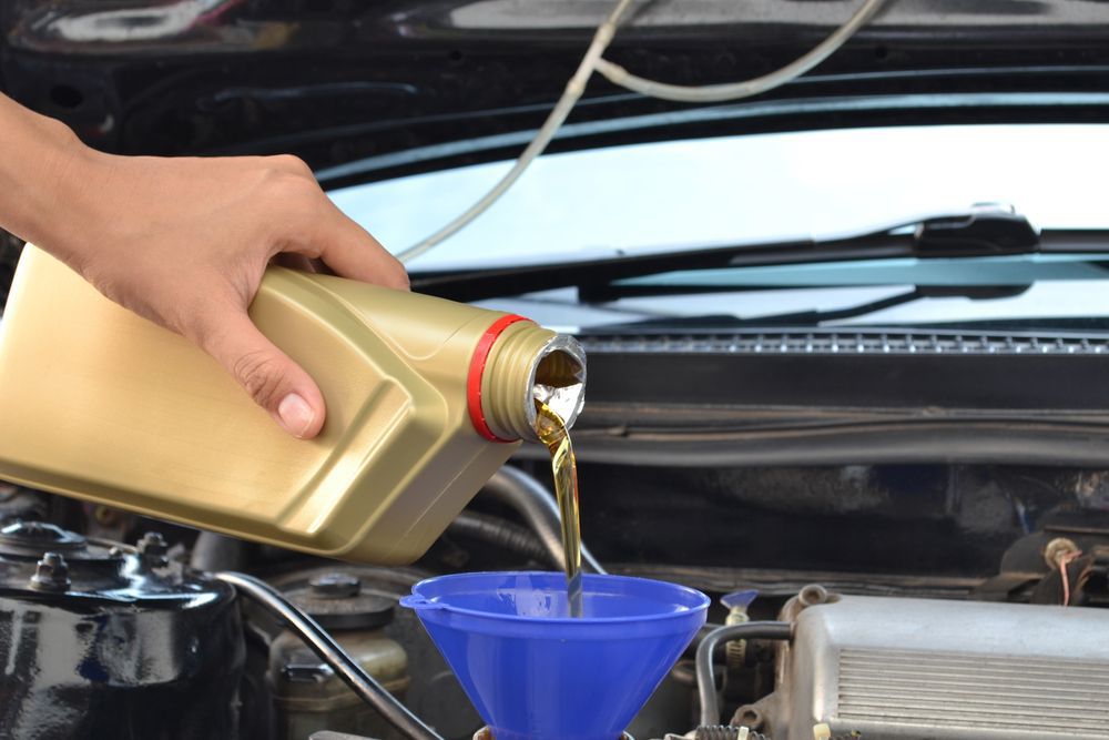 Car servicing mechanic pouring oil to engine — A Grade Oils & Batteries In Wodonga VIC