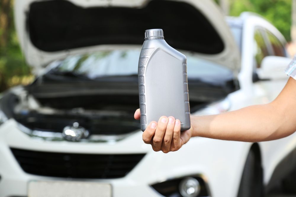 Motor oil in hand with white car background — A Grade Oils & Batteries In Benalla VIC
