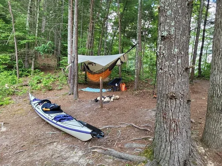 A kayak is parked next to a hammock in the woods.