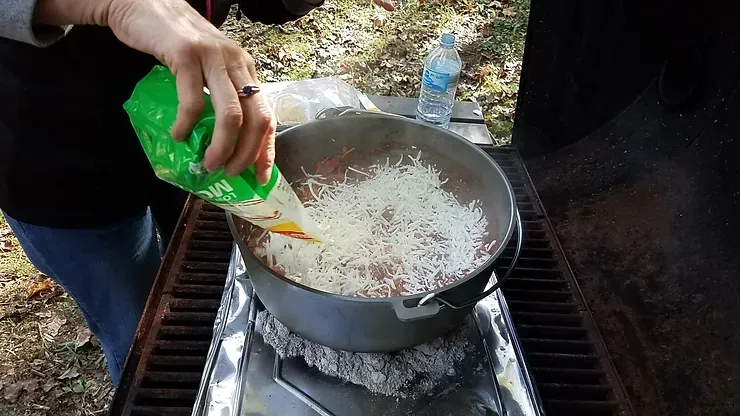 A person is pouring rice into a pot on a stove.