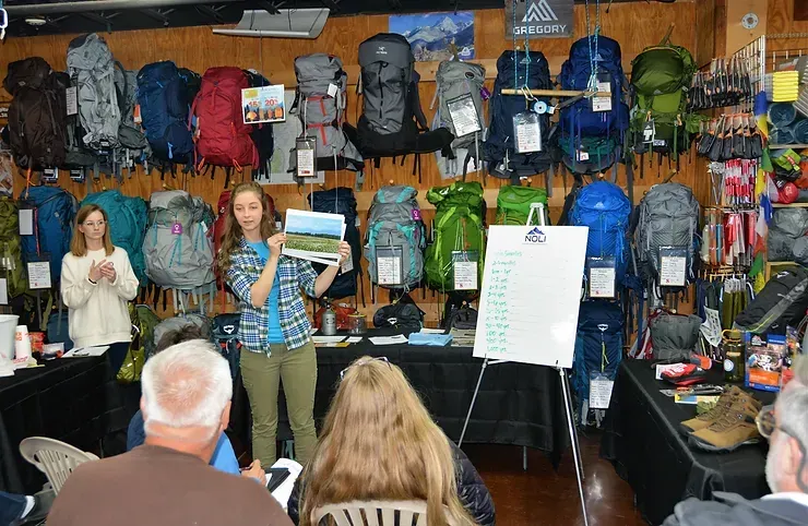 A woman is giving a presentation in front of a group of people in a store.