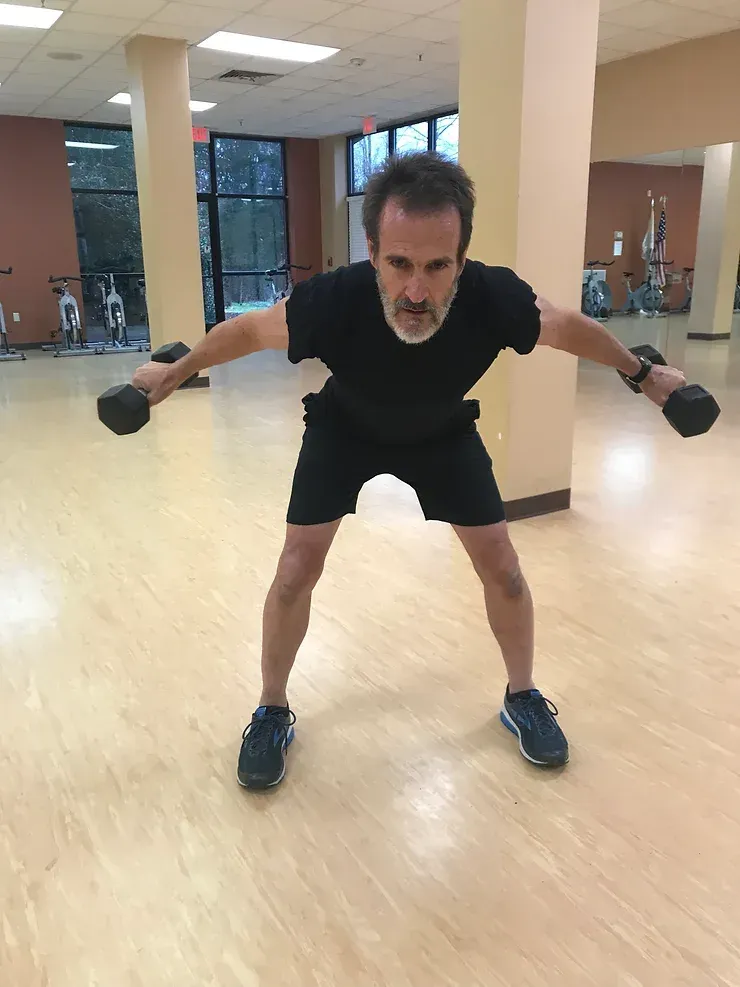 A man is holding a pair of dumbbells in a gym.