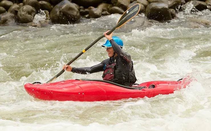 A person is paddling a red kayak in a river.