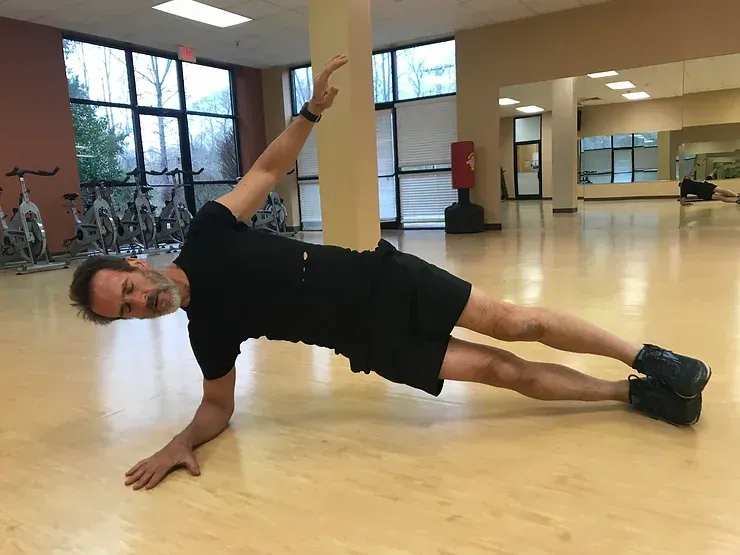 A man is doing a side plank in a gym.