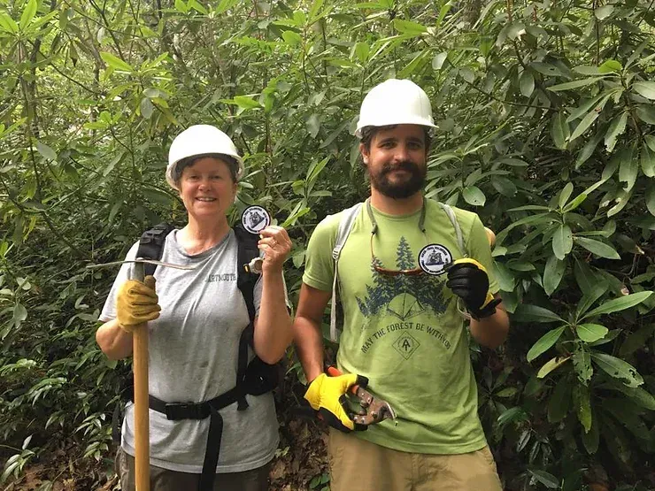 A man and a woman are standing next to each other in the woods.