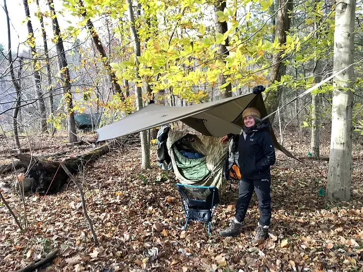 A person is standing next to a tent in the woods.