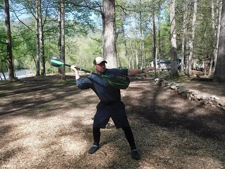 A man is swinging a baseball bat in the woods.