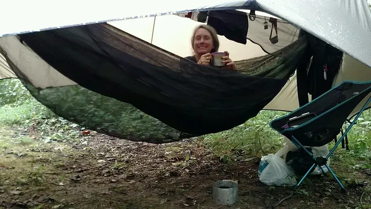 A woman is sitting in a hammock holding a cup of coffee.
