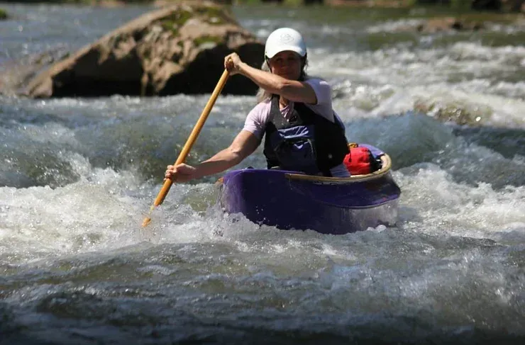 A woman is paddling a purple kayak through a river.