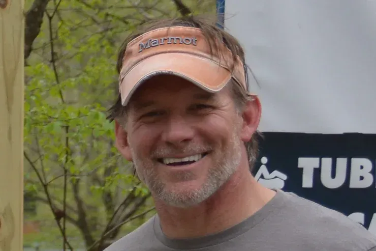 A man wearing a hat and a gray shirt is smiling in front of a tub sign.