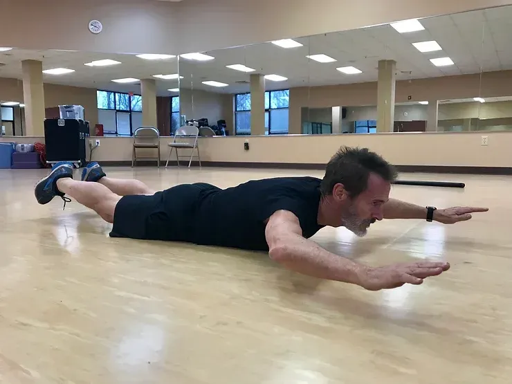 A man is laying on his stomach on a wooden floor in a gym.