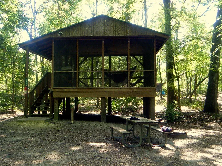A small house with a screened in porch and a picnic table in the woods