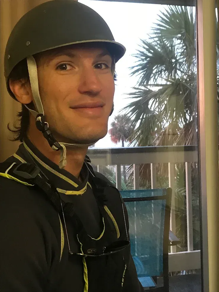 A man wearing a helmet is smiling in front of a window