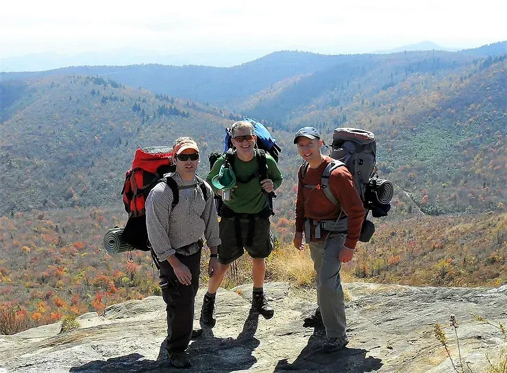 Three men with backpacks are standing on top of a mountain.