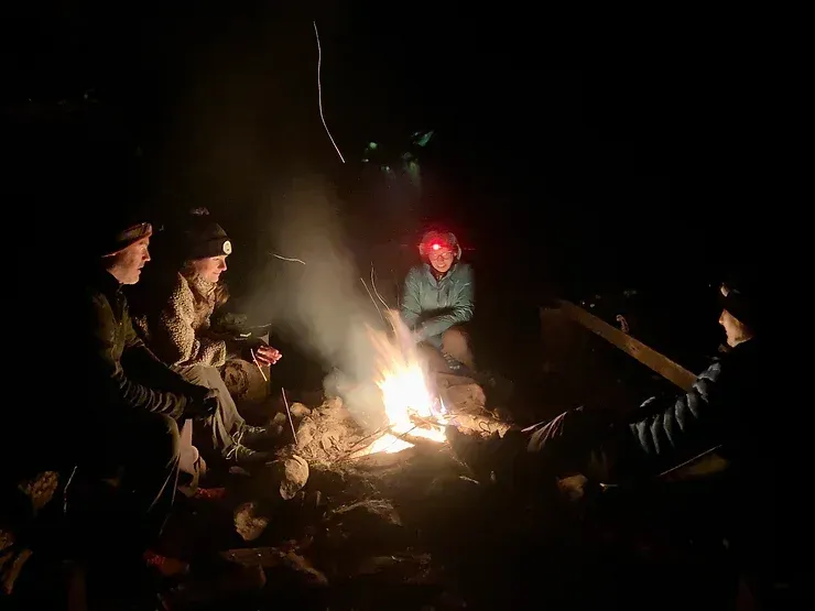 A group of people are sitting around a campfire at night.