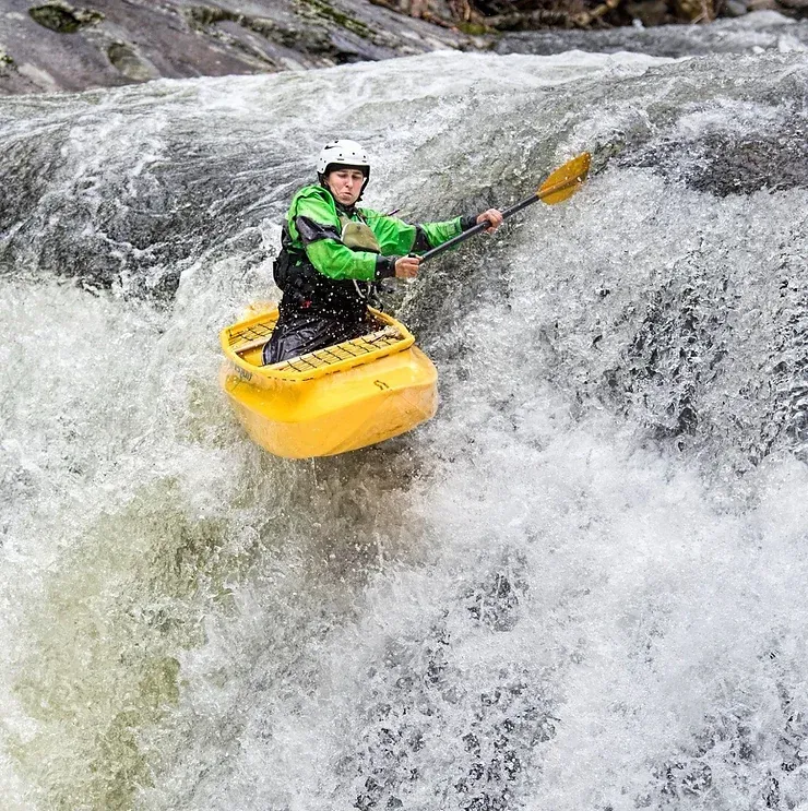 A man in a yellow kayak is paddling down a waterfall.