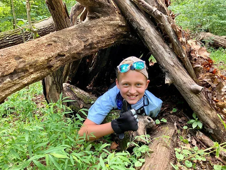 A young boy is peeking out of a wooden hut in the woods.
