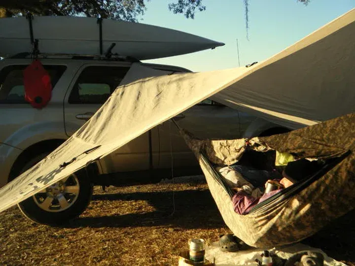 A hammock is sitting under a tarp next to a truck