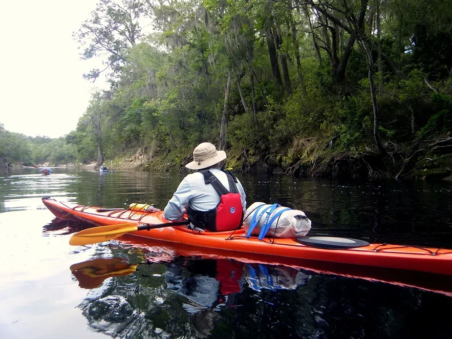 A man is sitting in an orange kayak on a river.