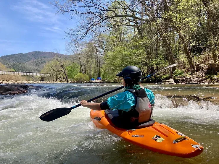 A person is paddling an orange kayak down a river.