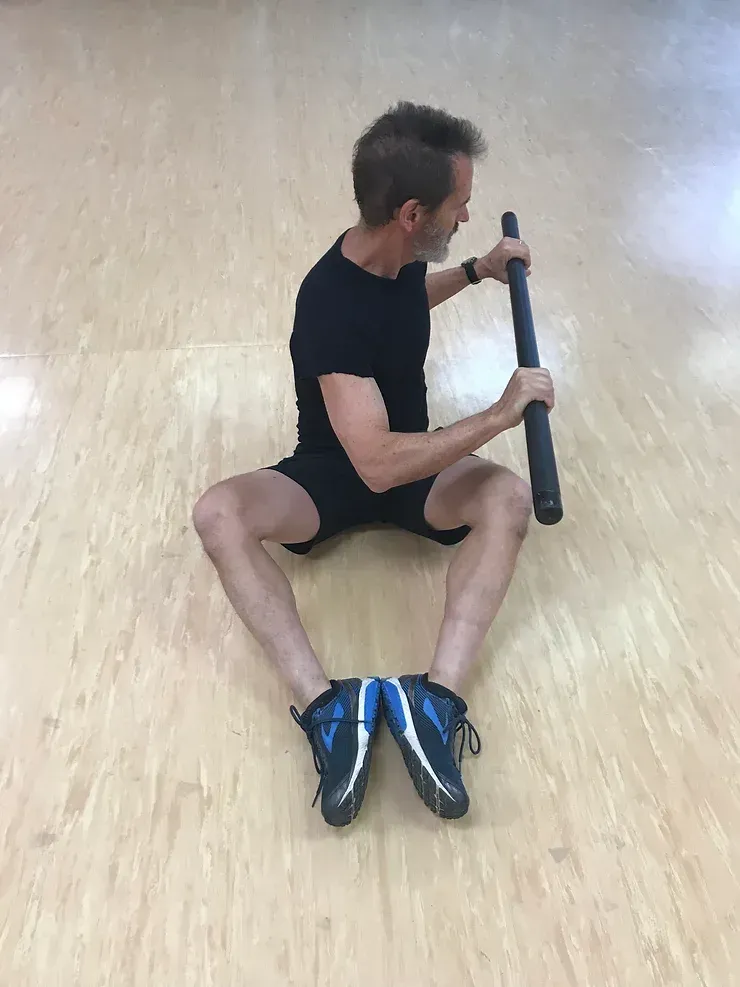 A man is sitting on the floor holding a barbell.