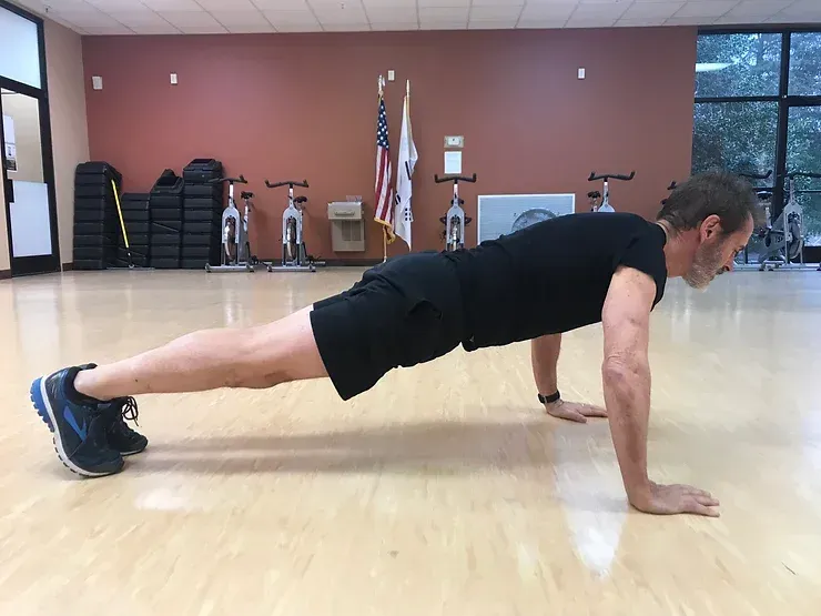 A man is doing push ups on a wooden floor in a gym.