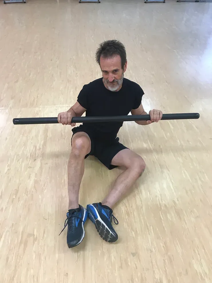 A man is sitting on the floor holding a barbell.
