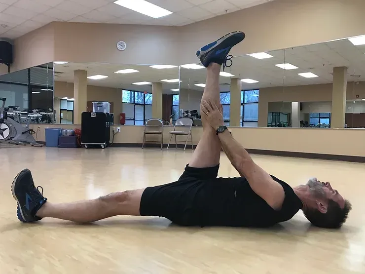 A man is laying on the floor stretching his legs in a gym.
