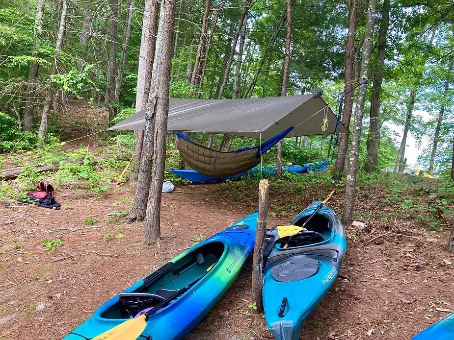 Two blue kayaks are parked next to a hammock in the woods.