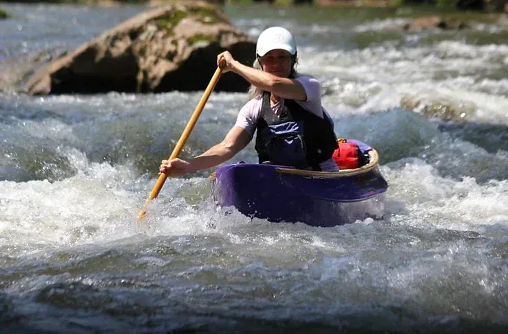 A woman in a purple kayak is paddling through a river