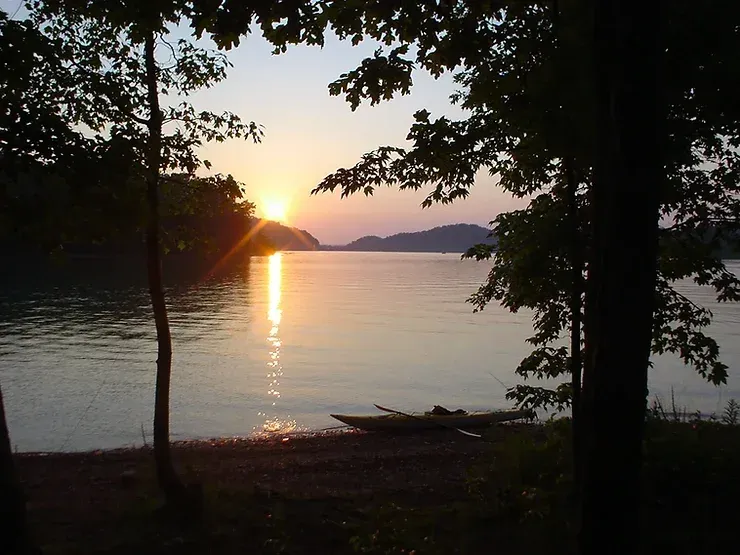 A kayak sits on the shore of a lake at sunset