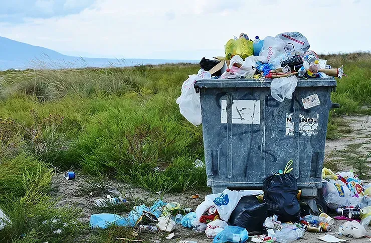 A garbage can is filled with trash in a field.