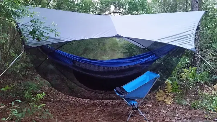 A hammock with a chair underneath it in the woods.
