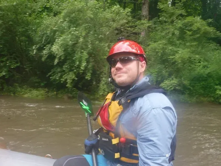 A man wearing a helmet and sunglasses is sitting in a raft on a river.