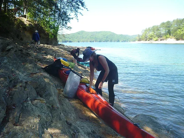 A woman is loading a red kayak into the water