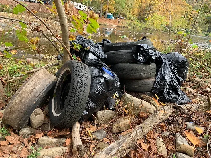 A pile of tires and trash bags on the ground next to a river.