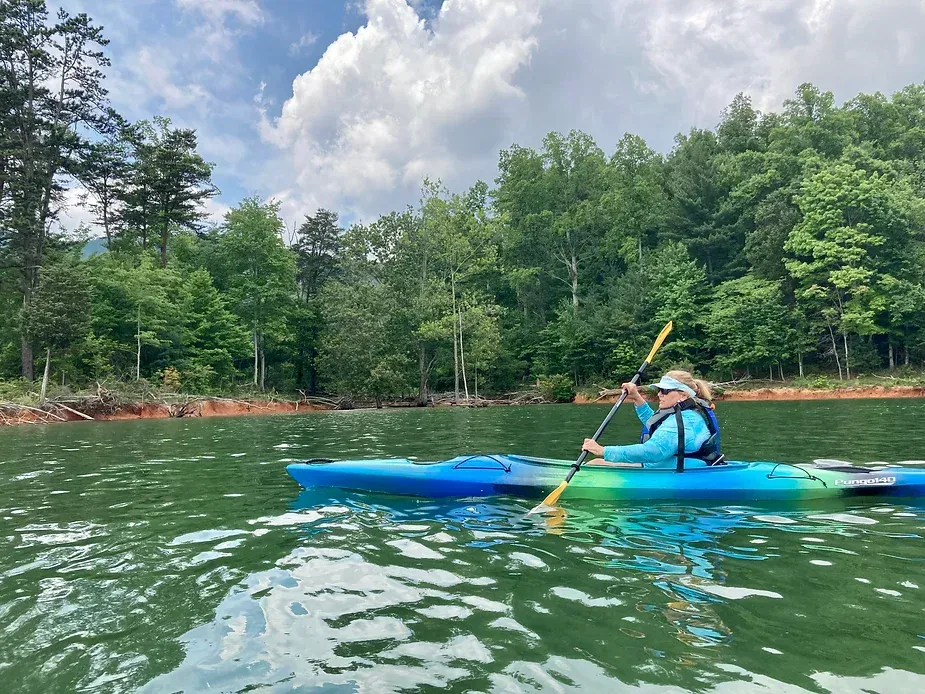 A woman is paddling a blue kayak on a lake.