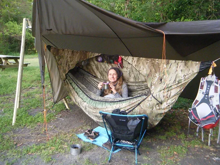 A woman is laying in a hammock under a tarp.