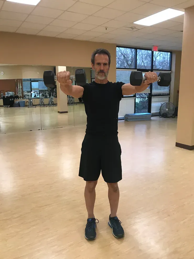 A man is holding a dumbbell over his shoulder in a gym.