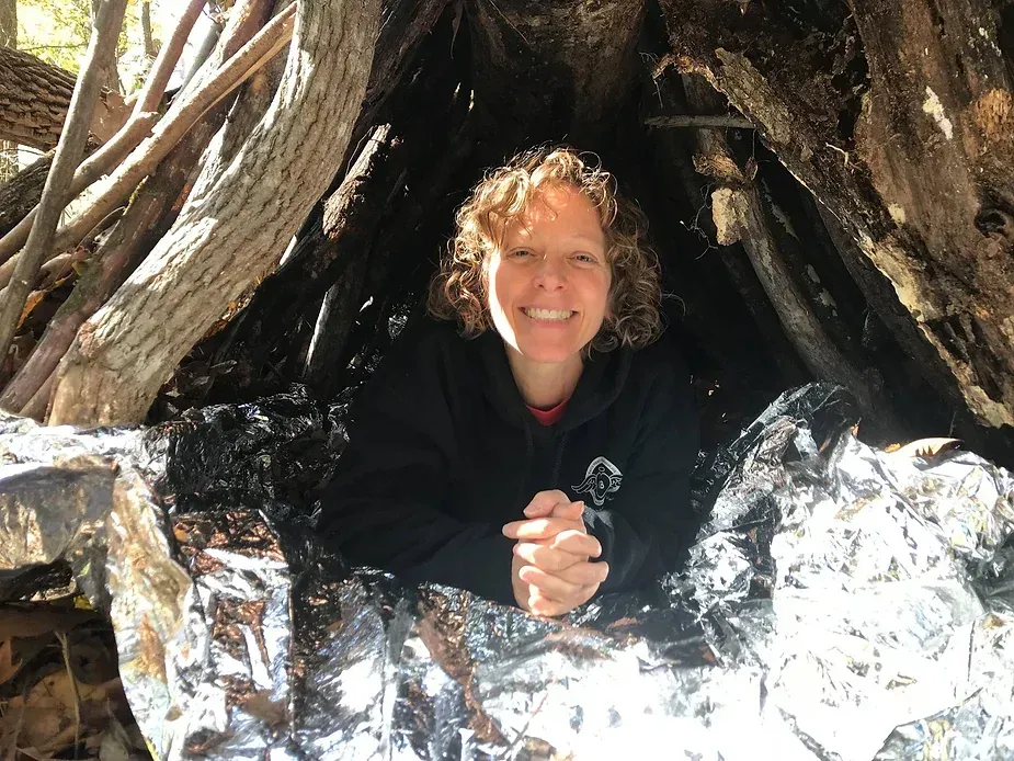 A woman is sitting in a shelter made of branches and aluminum foil.