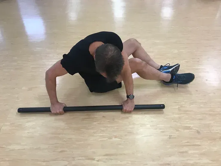 A man is doing push ups on the floor with a bar.