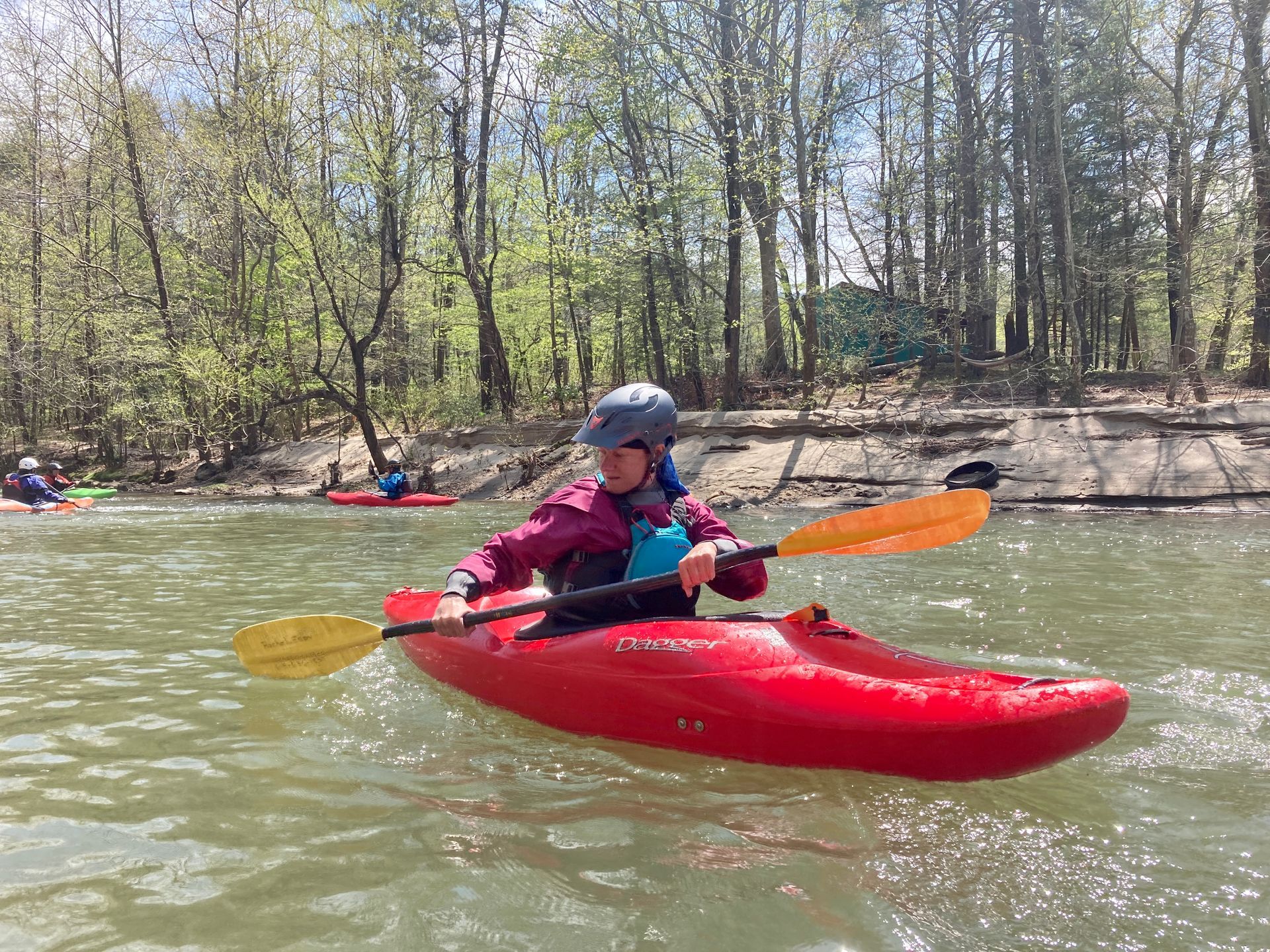 A woman is paddling a red kayak on a river.