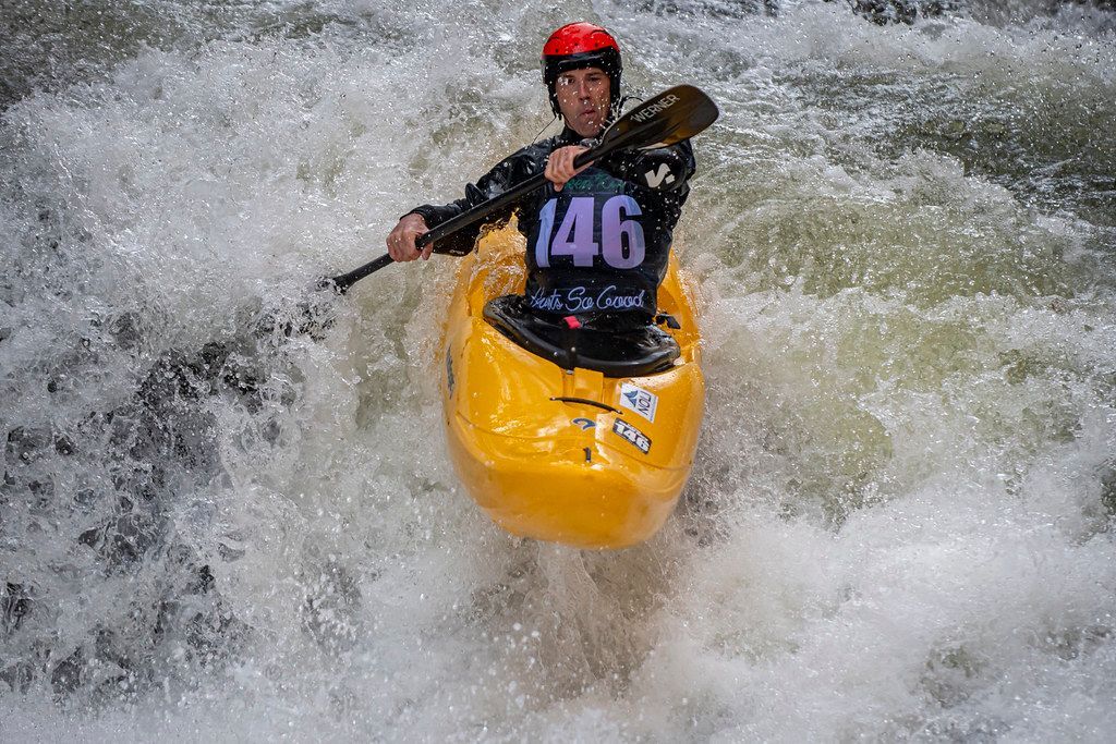 A man in a yellow kayak is paddling through a river.