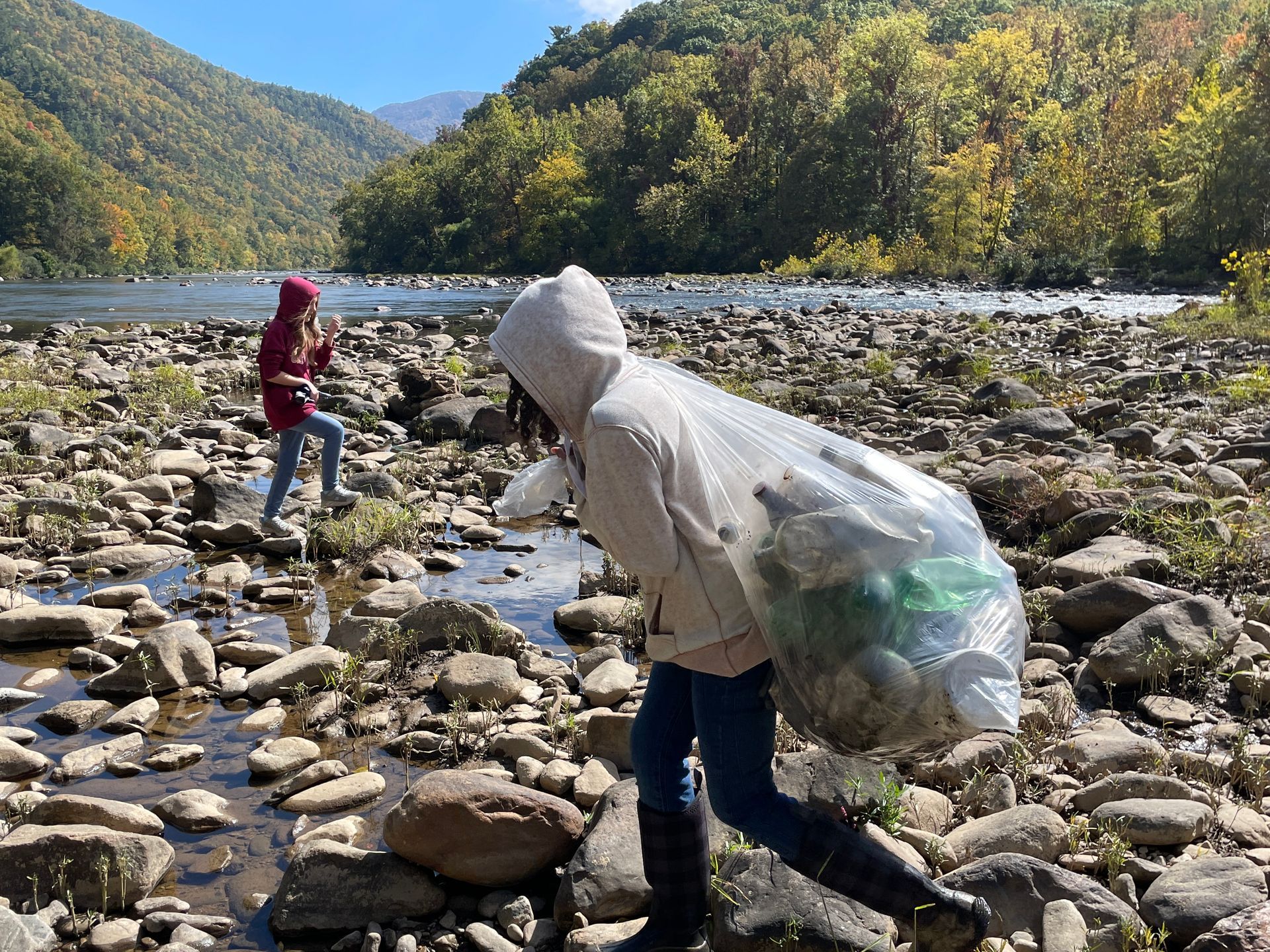 A woman is carrying a bag of trash across a rocky river.