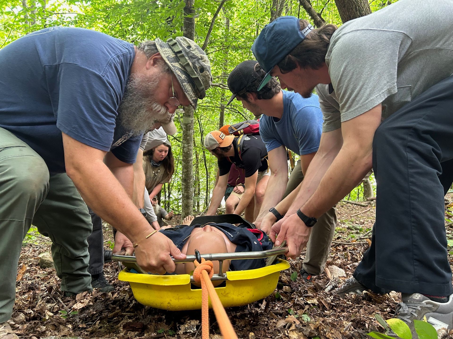 A group of men are helping a person on a stretcher in the woods.