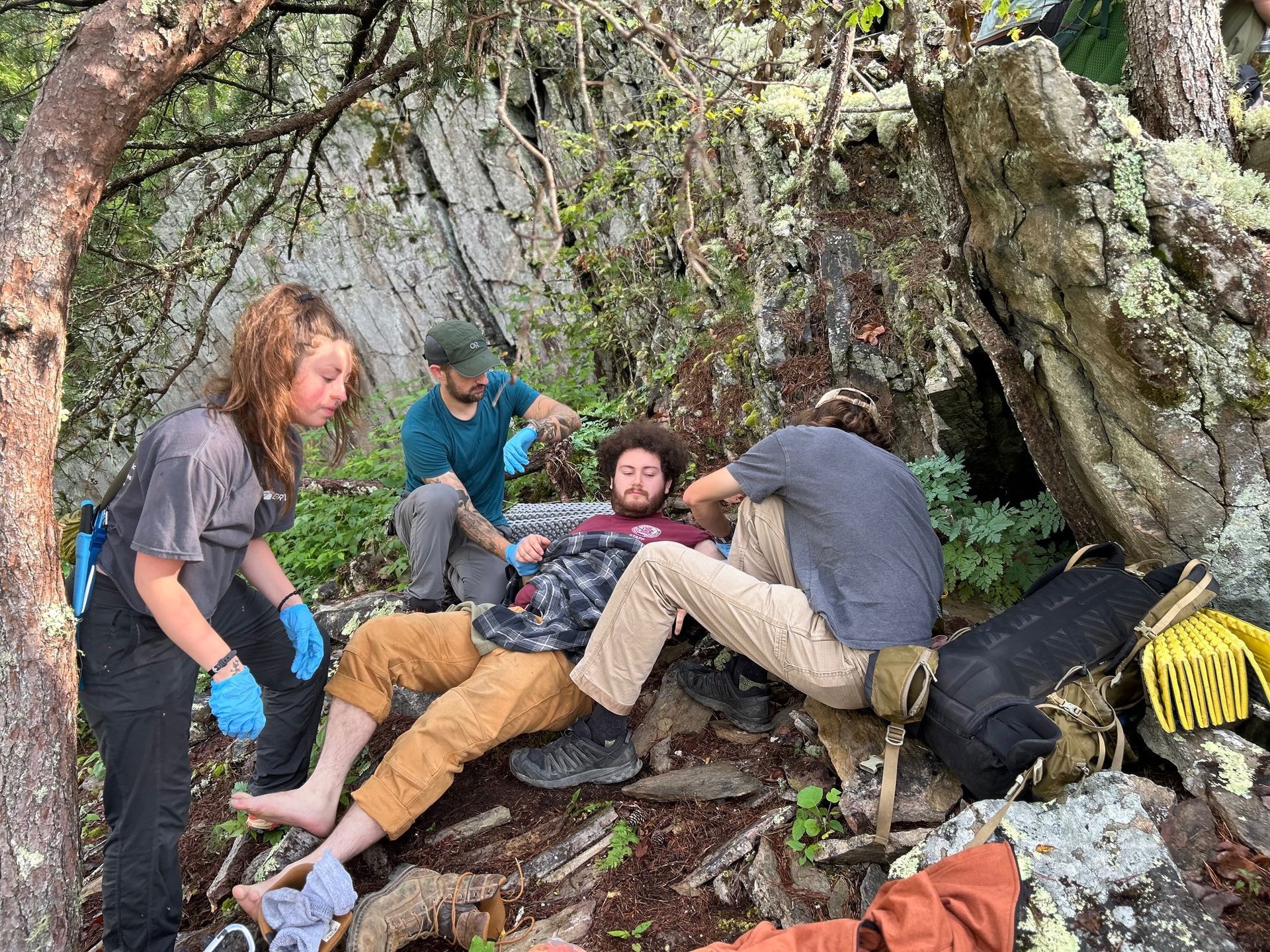 A group of people are helping a man who is laying on the ground in the woods.